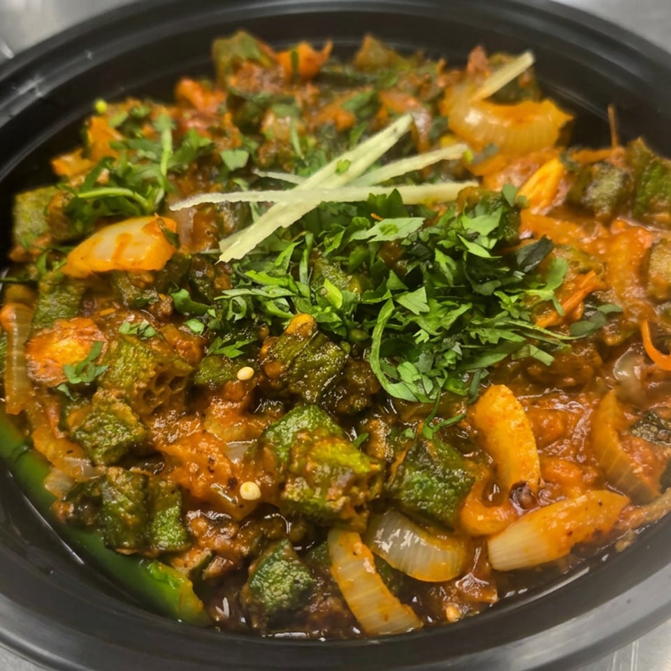 Black bowl of spiced mixed vegetables in reddish sauce, garnished with cilantro and ginger strips.