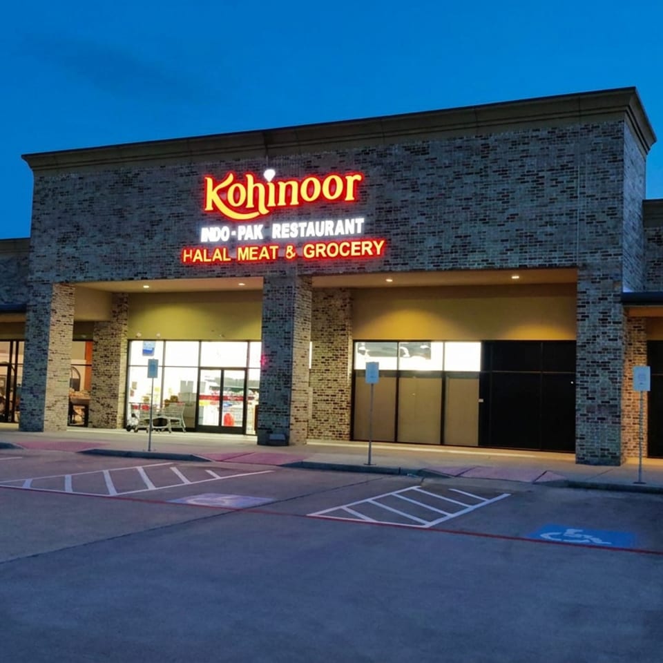 Kohinoor Indo-Pak restaurant, halal meat, and grocery storefront illuminated at dusk in a shopping center.