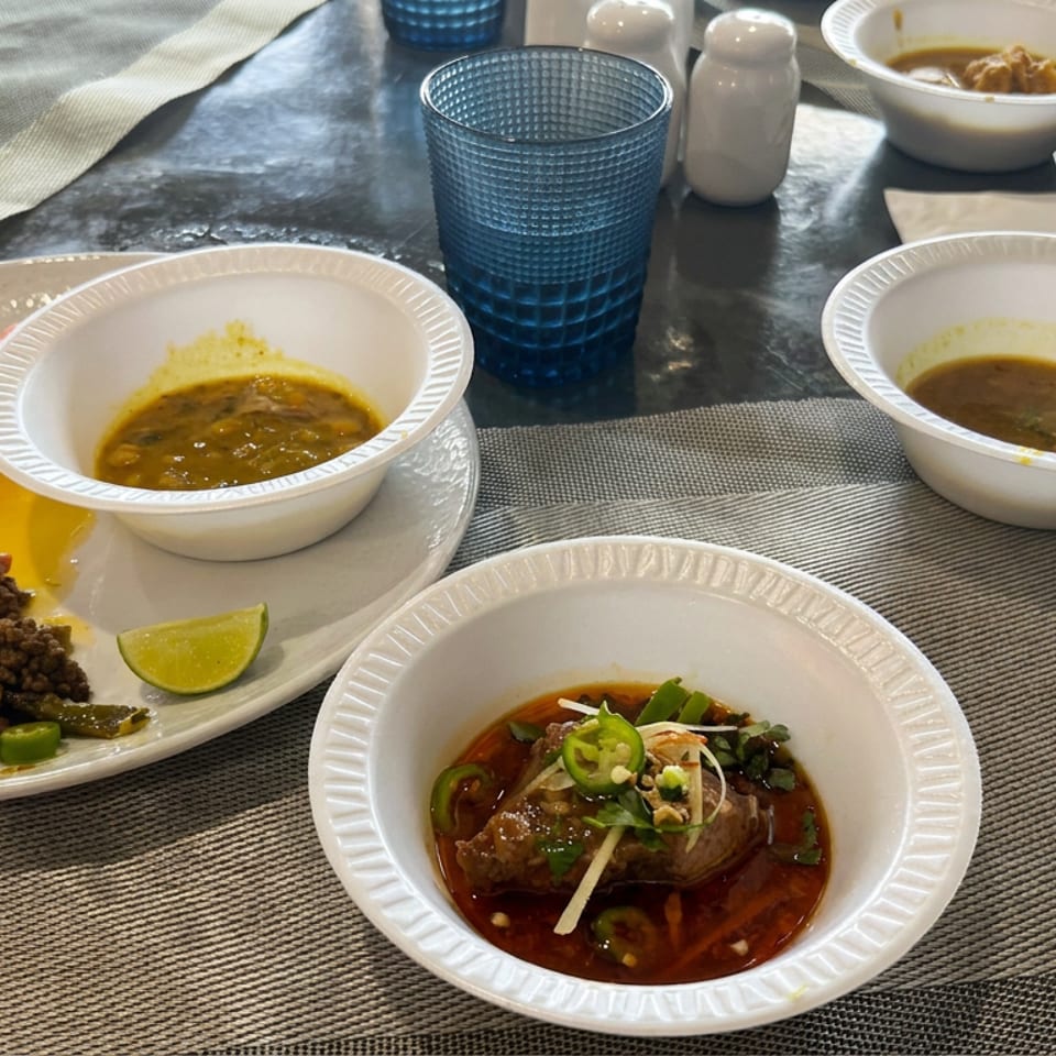 A tabletop displays bowls of sauces and stew, a plate of lentils with chutneys, lime, blue glasses, and condiments.