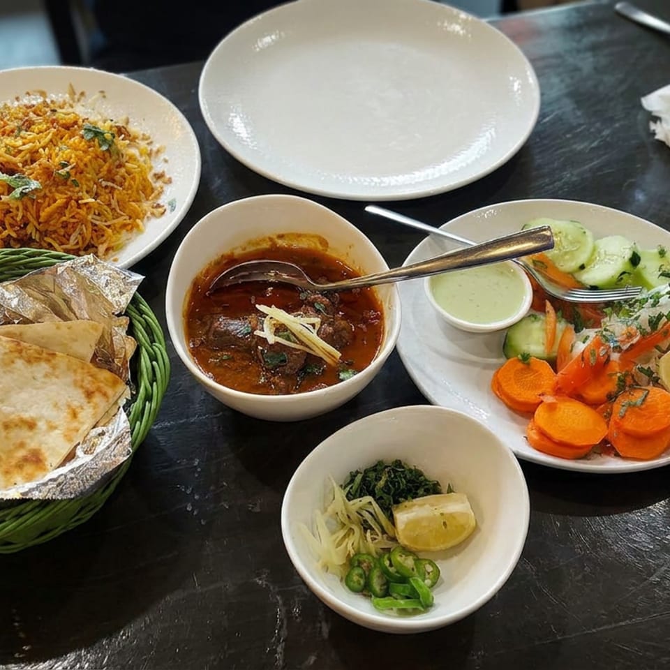 Indian meal spread with biryani, naan, curry, salad, chutney, sliced vegetables, and condiments on a dark dining table.