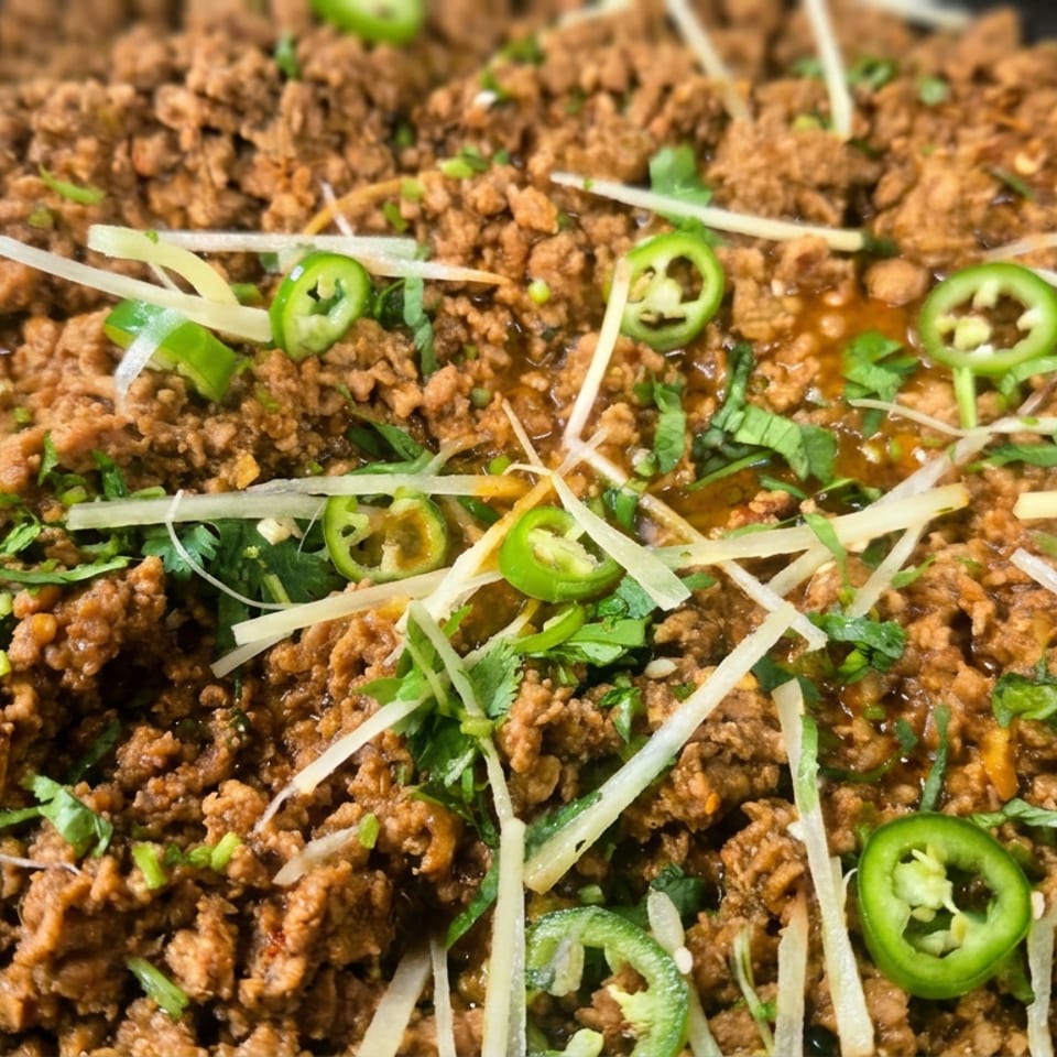 Spiced minced meat dish garnished with sliced green chilies, shredded ginger, cilantro, and scallions.