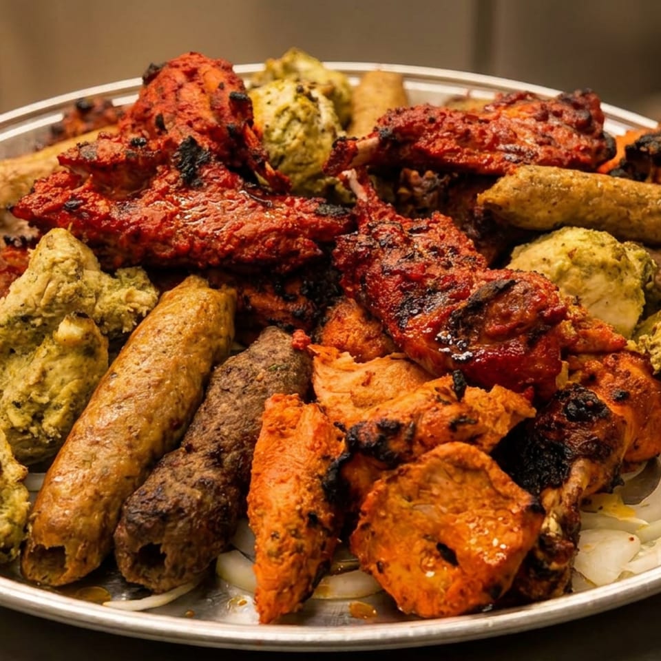 Large platter of assorted grilled Indian kebabs and tandoori meats arranged over sliced onions.