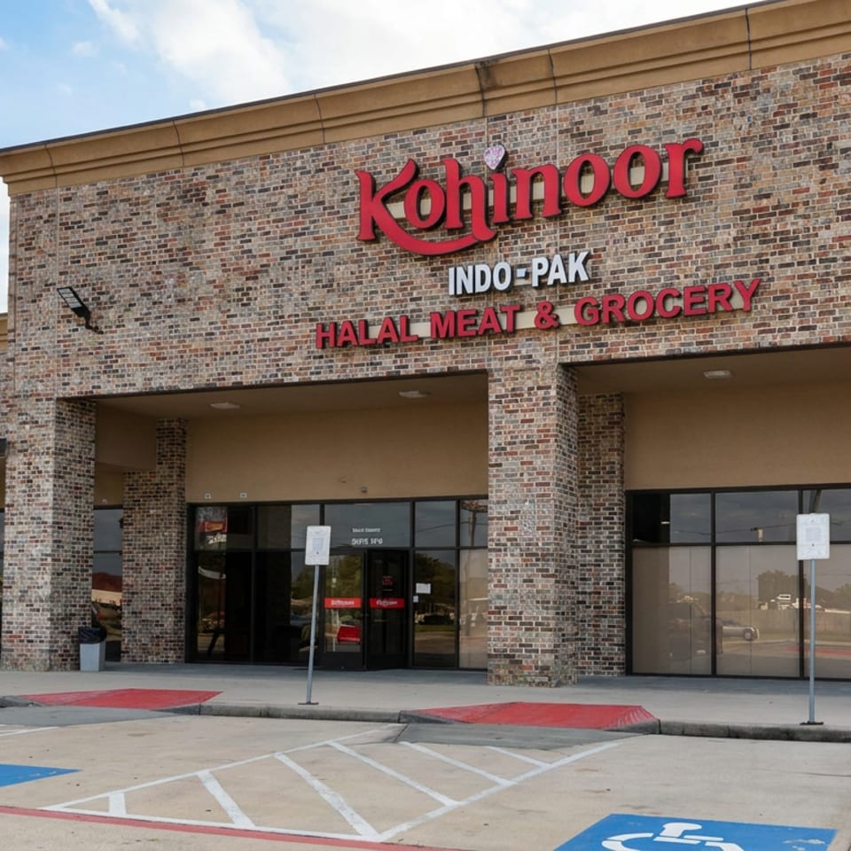 Kohinoor Indo-Pak halal meat and grocery storefront beside its restaurant entrance, with brick facade, parking lot, and blue skies.