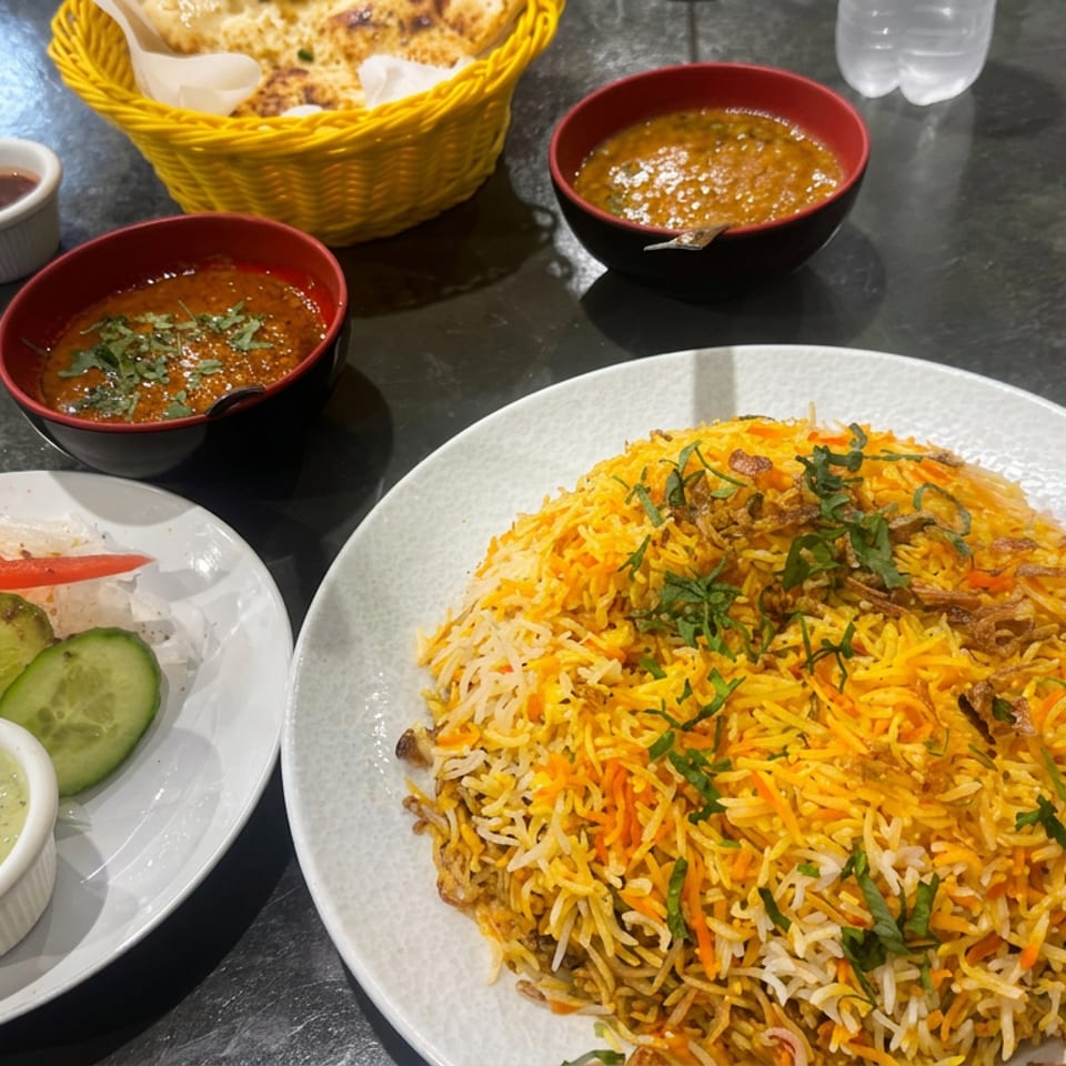 Indian biryani platter with saffron rice, cucumber and carrot salad, chutney, lentil soups, and naan on a restaurant table.